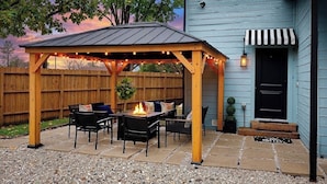 Une terrasse couverte avec un foyer, des sièges d’extérieur et une clôture en bois.