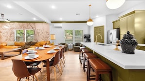 Une cuisine moderne dotée d’un îlot central, de tabourets de bar et d’un coin repas avec une longue table et des chaises.