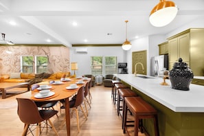 A modern kitchen with a central island, bar stools, and a dining area with a long table and chairs.