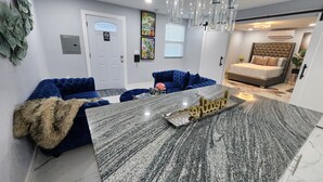 Een moderne woonkamer met een centraal gelegen eiland, een blauwe bank en een bed met een gestapeld hoofdbord.