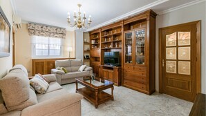 Una sala de estar con un sofá, una mesa de centro, un televisor y un aparador de madera con puertas de vidrio.