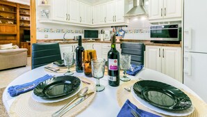 Una cocina moderna con armarios blancos, una mesa de comedor lista para cuatro personas y un televisor sobre la encimera.