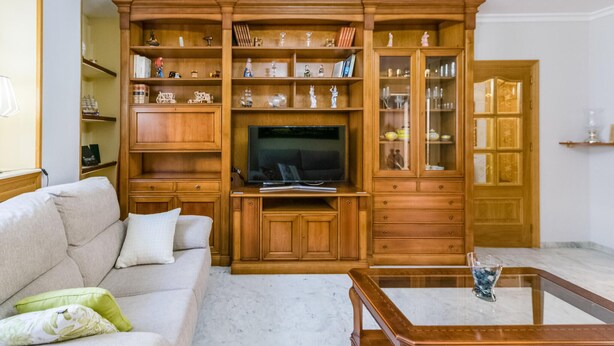 Una sala de estar con sofá, mesa de centro, mueble de entretenimiento de madera y televisor.