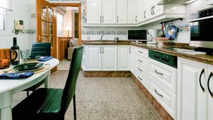 Una cocina con gabinetes blancos, una mesa de comedor con sillas, un televisor y un microondas.