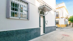 Un edificio con fachada blanca, base de mármol verde, ventana con reja de metal y puerta con un pequeño toldo encima.