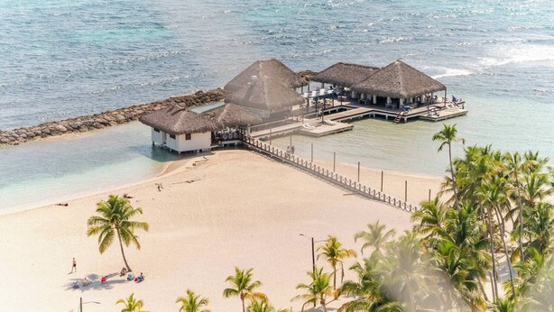 An overwater bungalow with thatched roofs, a sandy beach, and clear blue water. - Spacious Apto With Spectacular Views Of The Beach (Guayacanes)