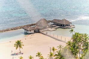 An overwater bungalow with thatched roofs, a sandy beach, and clear blue water.