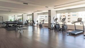 A spacious gym with various cardio machines, weightlifting equipment, and large windows offering views of the city. - Spacious Apto With Spectacular Views Of The Beach (Guayacanes)