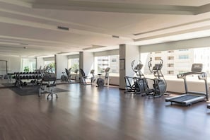 Ett rymligt gym med olika konditionsmaskiner, styrketräningsutrustning och stora fönster med utsikt över staden.