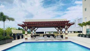 A swimming pool with a pergola and lounge chairs, surrounded by a high-rise building. - Spacious Apto With Spectacular Views Of The Beach (Guayacanes)