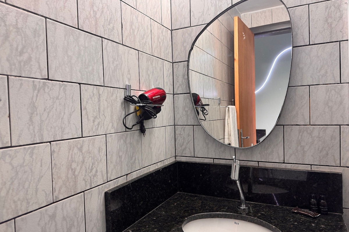 A bathroom with a black countertop sink, a mirror, and a hairdryer mounted on the wall.