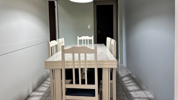 A dining area with a rectangular table and six chairs, a hanging light fixture, and a door leading to another room. - Ancoragem (Bombinhas)