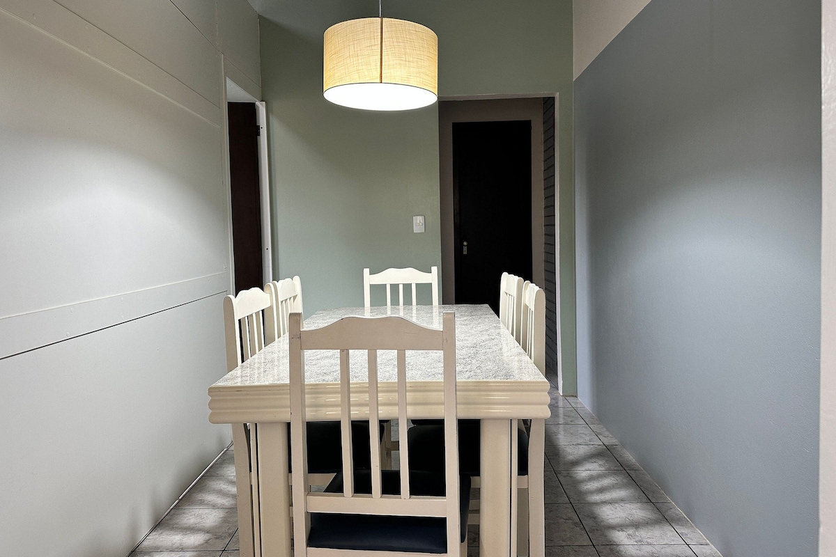 A dining area with a rectangular table and six chairs, a hanging light fixture, and a door leading to another room.