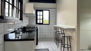 A kitchen with a gas stove, a sink, and a window. There are bar stools and a door leading to another room. - Ancoragem (Bombinhas)