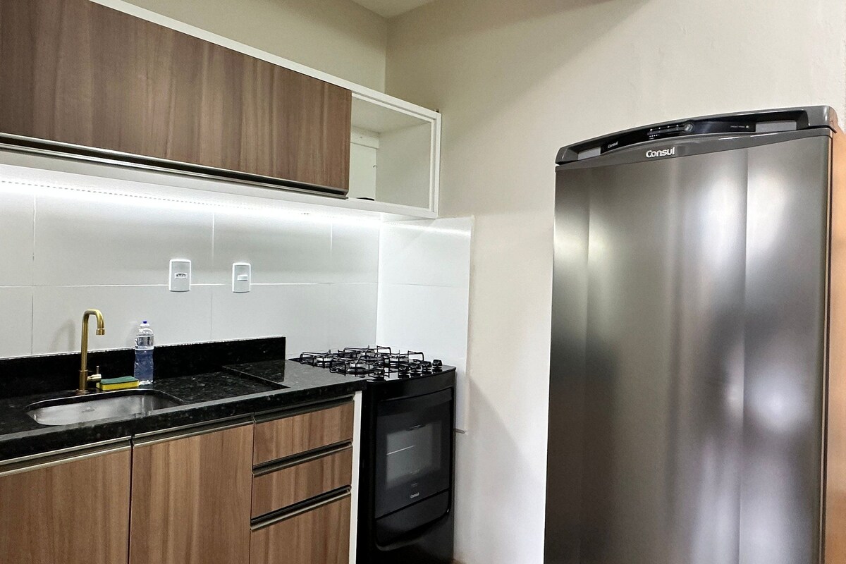 A modern kitchen with wooden cabinets, a stainless steel refrigerator, a gas stove, and a sink with a faucet.