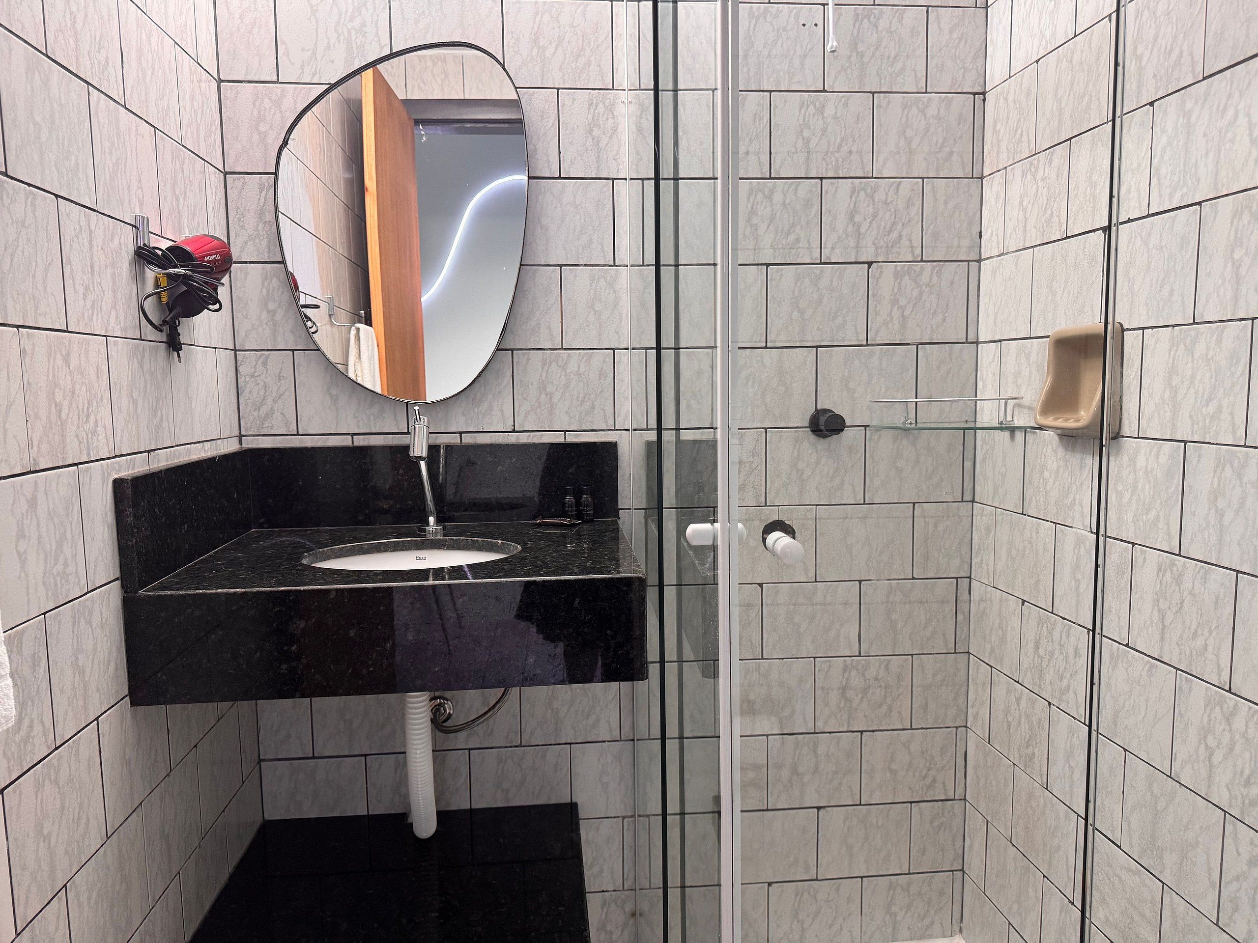 Ett modernt badrum med en svart tvättställ, en spegel och en duschavdelning med glasväggar.