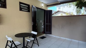 A balcony with a table and chairs, a door, and a view of the street.