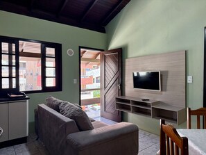 A living room with a sofa, TV, and a dining area. - Ancoragem (Bombinhas)