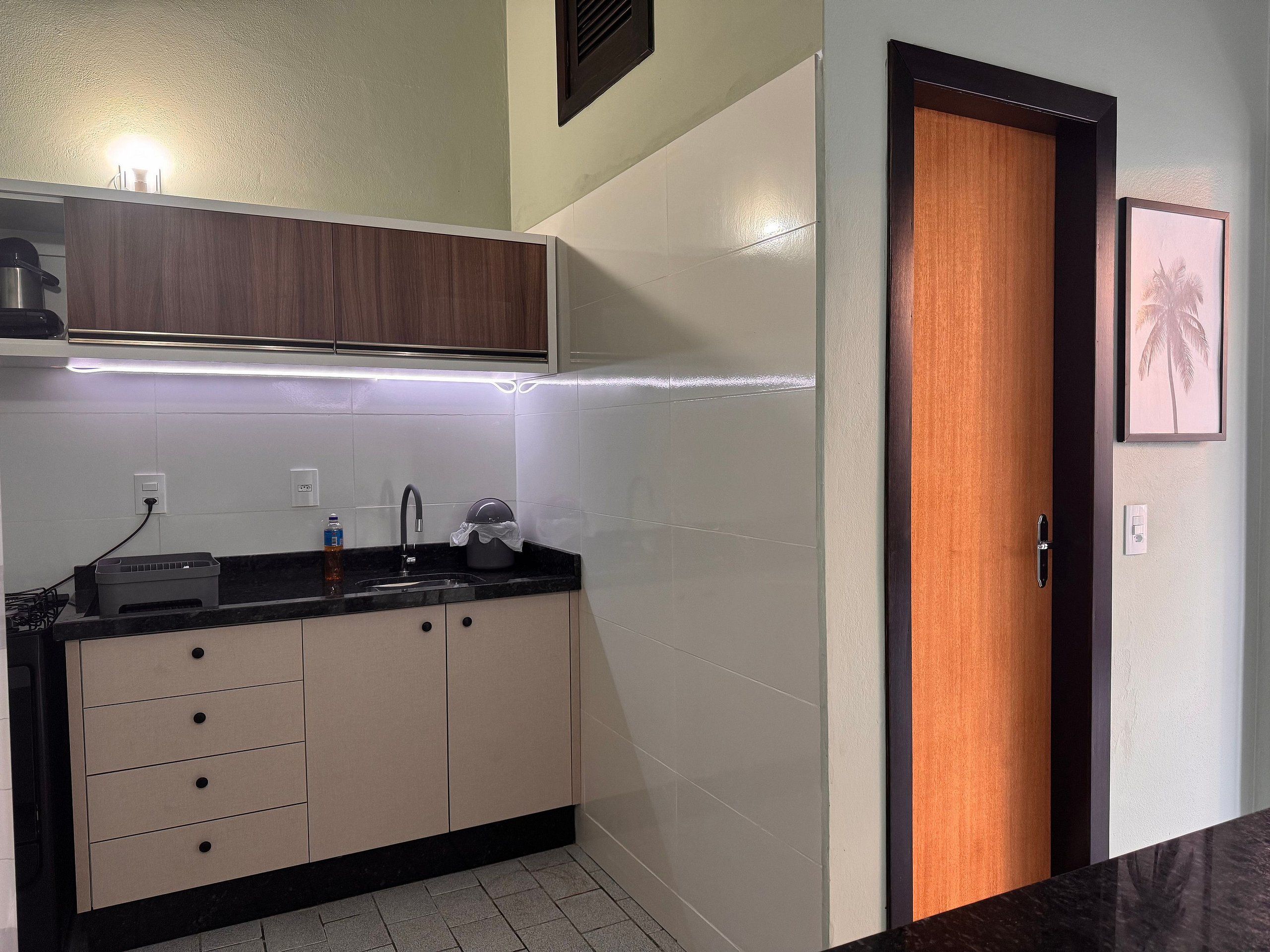 Uma cozinha moderna com bancada preta, armários bege e porta de madeira.