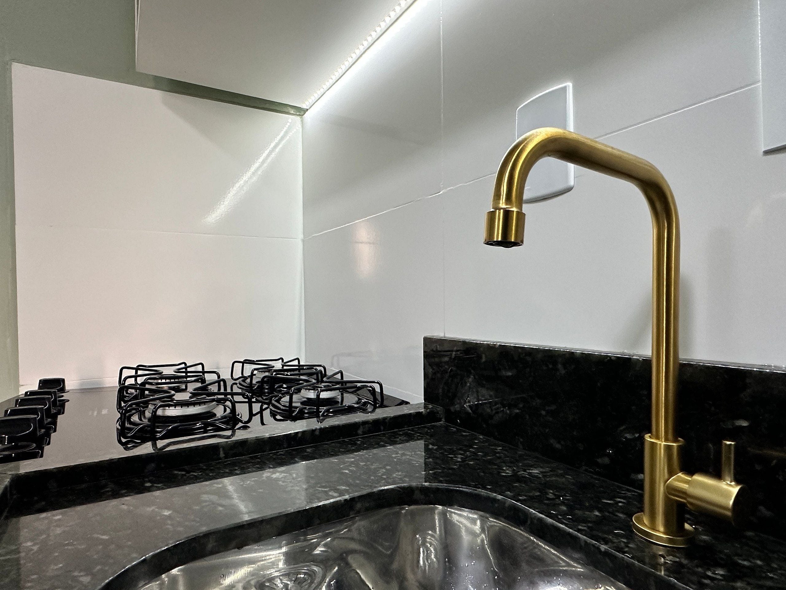 Een keuken met een gasfornuis, een spoelbak en een gouden kraan.