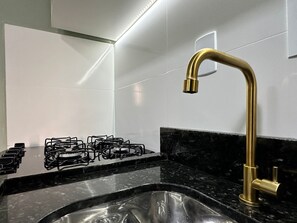 Una cocina con estufa a gas, un lavamanos y un grifo dorado.