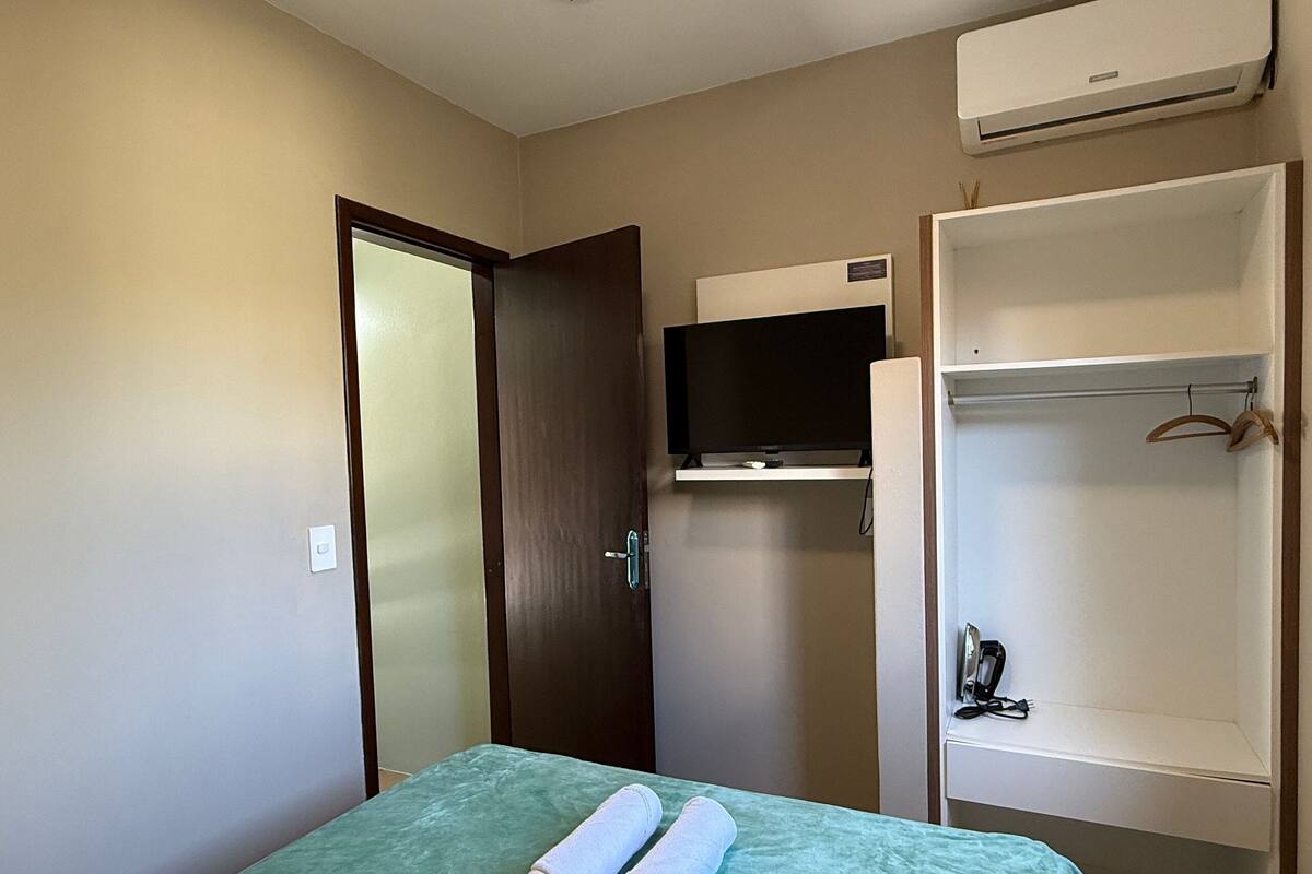 Ein Hotelzimmer mit einem Bett, einem an der Wand befestigten Fernseher, einem Kleiderschrank und einer Klimaanlage.