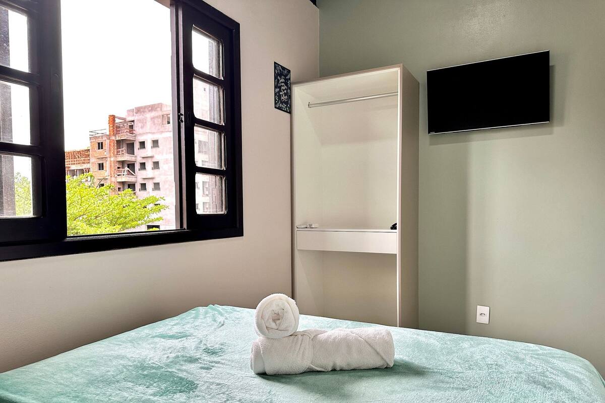 Ein Zimmer mit einem Bett, einem Fenster, einem weißen Schrank und einem Flachbildfernseher an der Wand.