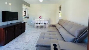 A living room with a television, a sofa, a dining table with chairs, and a ceiling fan. - Ancoragem (Bombinhas)