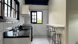 A kitchen with a gas stove, a sink, and a window. There are bar stools and a door leading to another room. - Ancoragem (Bombinhas)