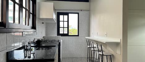 Een keuken met een gasfornuis, een gootsteen en een raam. Er staan barkrukken en een deur die naar een andere kamer leidt.