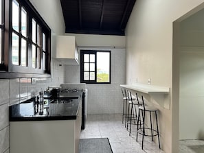 A kitchen with a gas stove, a sink, and a window. There are bar stools and a door leading to another room. - Ancoragem (Bombinhas)