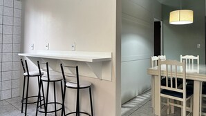 A modern kitchen with a white countertop, black bar stools, and a dining table with white chairs. - Ancoragem (Bombinhas)