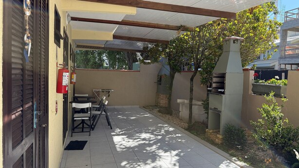 A covered patio area with a barbecue grill, a fire extinguisher, and outdoor seating. - Ancoragem (Bombinhas)