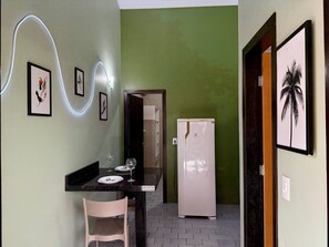 A compact kitchen with a dining area, a refrigerator, and a wall-mounted light fixture. - Ancoragem (Bombinhas)