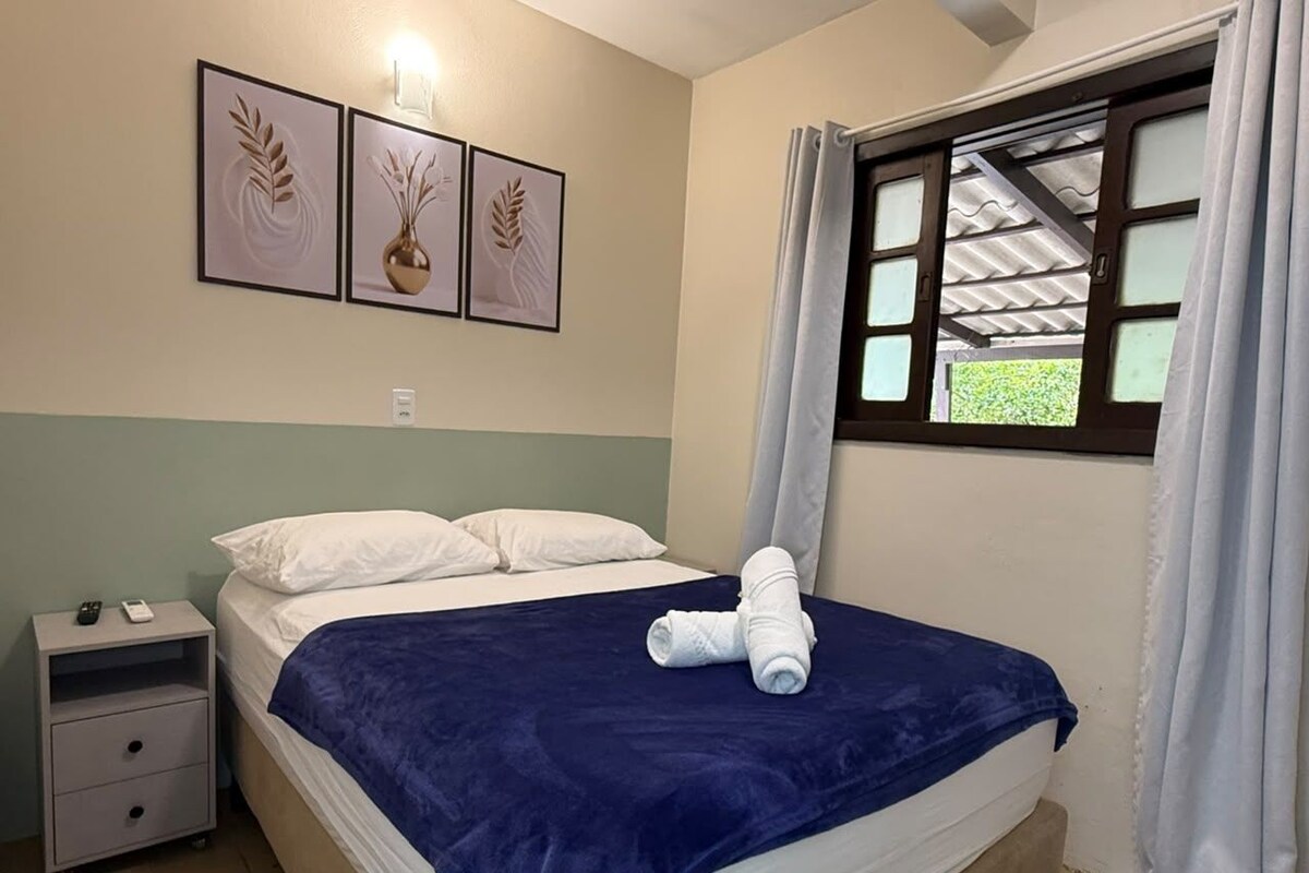 A hotel room with a bed, a nightstand, a window with curtains, and wall art.