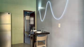 A compact kitchen with a refrigerator, a dining table with chairs, and a wall-mounted light fixture.