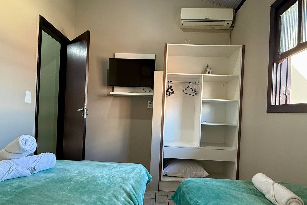 Ein kleiner, ordentlicher Raum mit zwei Betten, einem Fernseher und einem Kleiderschrank.