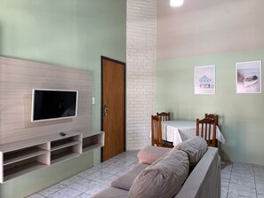 A living room with a flat-screen TV mounted on a wooden wall, a dining table with chairs, and a sofa. - Ancoragem (Bombinhas)