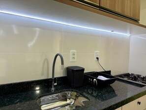 A modern kitchen with a stainless steel sink, a black trash bin, and a gas stove. - Ancoragem (Bombinhas)