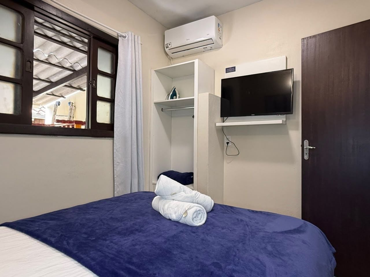 A hotel room with a bed, a TV mounted on the wall, and an air conditioning unit above the bed.