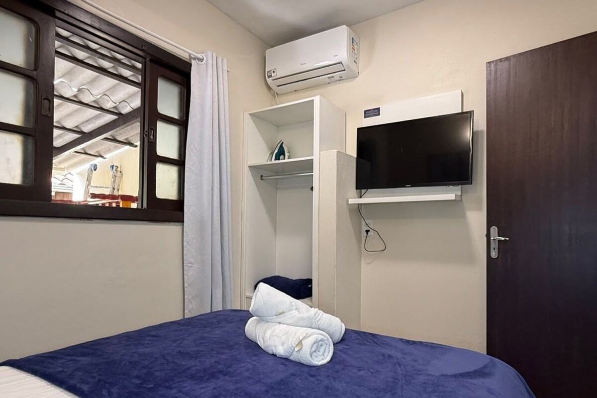 A hotel room with a bed, a TV mounted on the wall, and an air conditioning unit above the bed.
