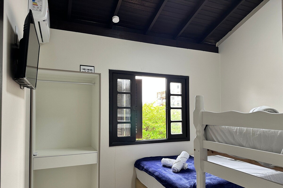 A small, clean room with a bunk bed, a window with a view of greenery, and a white wardrobe.