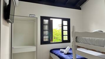 Een kleine, nette kamer met een stapelbed, een raam met uitzicht op groen en een witte garderobe.