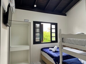 Una habitación pequeña y limpia con literas, una ventana que da a zonas verdes y un armario blanco.