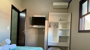 A small, neatly organized room with two beds, a television, and a wardrobe.