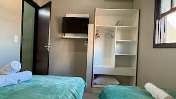 A small, neatly organized room with two beds, a television, and a wardrobe.