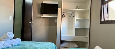 Una habitación pequeña y ordenada con dos camas, un televisor y un armario.