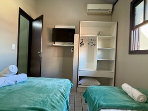 Una habitación pequeña y ordenada con dos camas, un televisor y un armario.