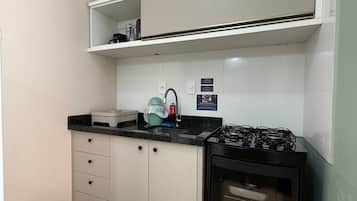 Uma cozinha compacta com fogão a gás, pia e micro-ondas. Há armários com gavetas e bancada.