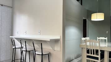 A modern kitchen with a white countertop, black bar stools, and a dining table with white chairs.